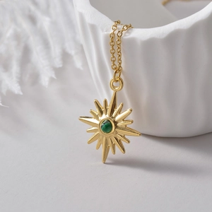 Gold eight-pointed star necklace with emerald green gemstone on a white ceramic tray