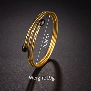 Detail of 5.5cm gold layered coil bracelet with black spherical ends on dark background