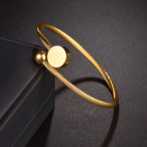 Detail of gold twisted cable cuff bracelet with metal disc and bead on jewelry box
