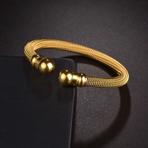 Detail of gold woven mesh cuff bracelet with polished bead ends on black textured background