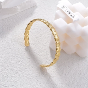 Detail of gold-plated stainless steel open bangle with leaf-like textured finish on stone