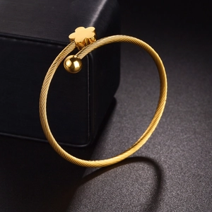 Gold stainless steel twisted cuff bracelet with flower and bead detail on jewelry box