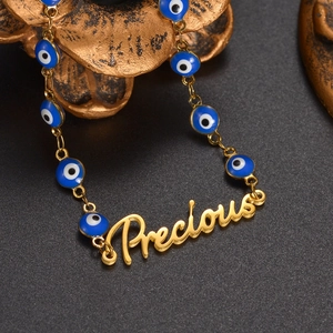 Golden necklace with blue evil eye beads and Precious letter pendant on dark background