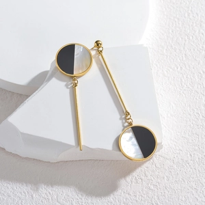 Asymmetric gold earrings with black and white shell discs displayed on white stone