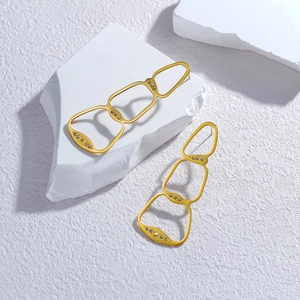 Golden hollow geometric drop earrings with sparkling rhinestones on textured stone