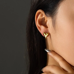 Detailed view of polished heart-shaped gold stud earring worn by a female model