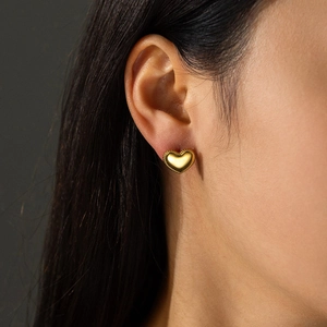 Macro shot of a golden heart stud earring with beaded edge detail on a model ear