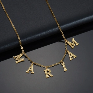 Collier en acier doré avec lettres MARIAM en strass sur un fond noir texturé