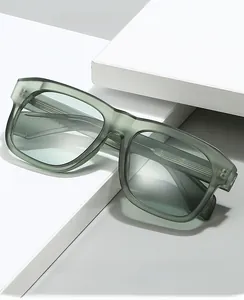 Détail de lunettes à monture carrée vert-gris translucide sur un bloc géométrique blanc