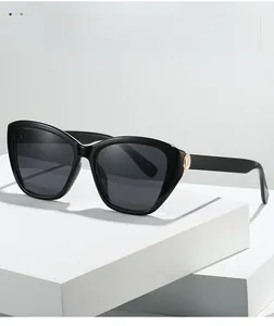 Detail of black cat-eye sunglasses featuring an oval gold metal hinge and polished frame