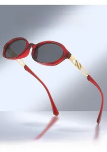 Detail of red oval sunglasses with gold metal temples and geometric engraving patterns