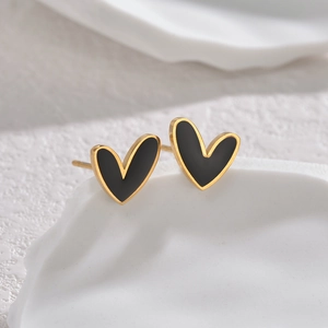 Macro view of gold heart stud earrings with black enamel on a textured white stone base