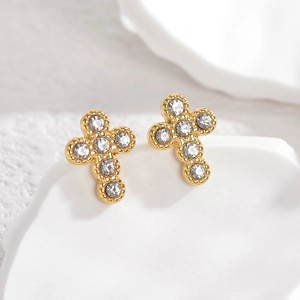 Macro shot of gold-plated cross earrings with clear crystal inlay on a white tray