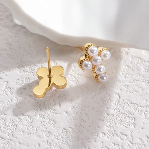 Minimalist gold cross earrings with white pearls on elegant white stone background