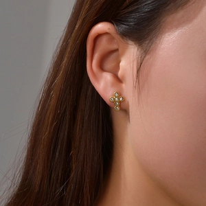 Close-up of a gold cross earring with zircon stones worn by a model in soft warm lighting