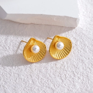 Macro shot of gold shell stud earrings with white pearl detail on textured stone