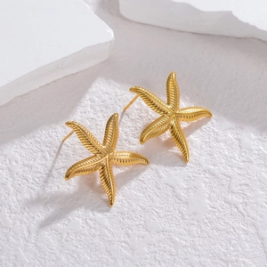 Minimalist gold starfish earrings with textured surface on a white stone background