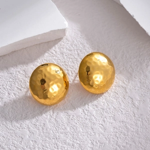 Minimalist golden hammered texture ball stud earrings shown on an artistic textured surface