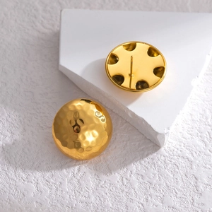 Textured hammered gold sphere stud earrings displayed on minimalist white props