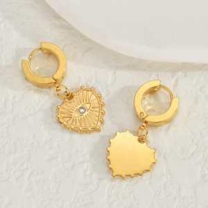 Boucles d'oreilles cœur dorées avec motif œil et zircone sur fond blanc texturé