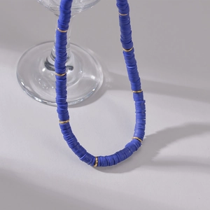 Macro detail of blue Heishi beads necklace with 14K gold-plated spacers on a glass base