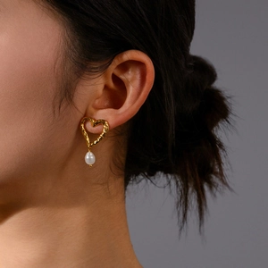 Detail eines goldenen Herz-Ohrrings mit weißer Perle, getragen von einem Model