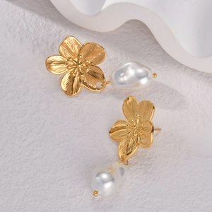 Elegante goldene Blumenohrringe mit Barockperlen auf einer weißen Steinoberfläche