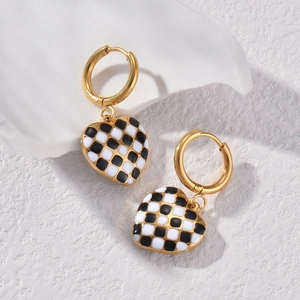 Checkerboard heart drop earrings with gold metal hoops on a white textured stone surface