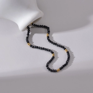 Vue macro d'un collier de perles noires facettées avec des accents dorés sur fond blanc
