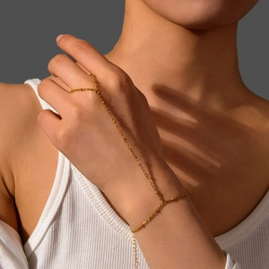 Détail d'un bracelet bague doré avec une fine chaîne à billes reliant la bague au poignet