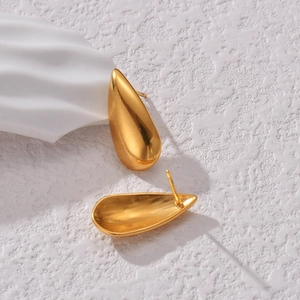 Elegant gold teardrop earrings with a polished mirror finish on a white textured stone