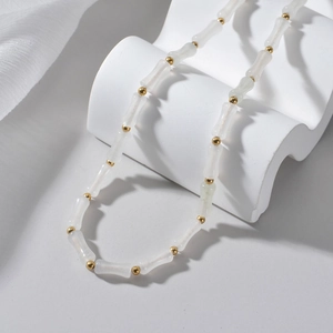 Detail of white bamboo beads and gold spacers on a minimalist necklace display