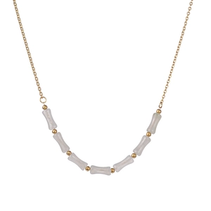 Minimalist gold stainless steel tube necklace with white bone-shaped beads in flat lay