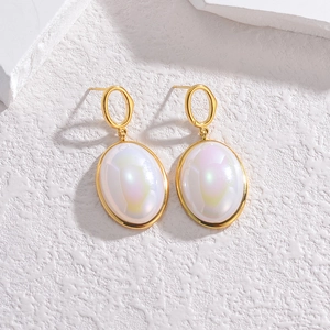 Detail of gold dangle earrings with iridescent oval stones on a white stone background