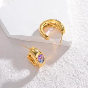 Detail of gold C-shaped earrings featuring a multifaceted iridescent color-changing gemstone