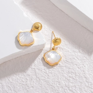 Detail of scalloped gold earrings with white mother-of-pearl shells on stone background