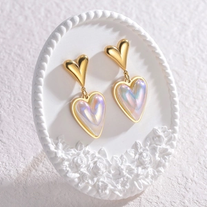 Golden double heart earrings with shimmering opal effect on elegant white floral stand