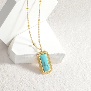 Golden stainless steel necklace with a rectangular turquoise pendant on white geometric block
