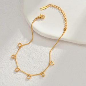 Detail eines vergoldeten Edelstahl-Armbands mit Zirkonia-Herzen auf weißen Steinplatten