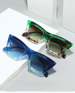 Close-up of retro cat-eye frames in green and blue gradient on a minimalist stand