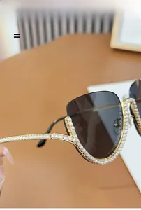 Detail of half-frame gold metal sunglasses with white pearl embellishments and grey lenses