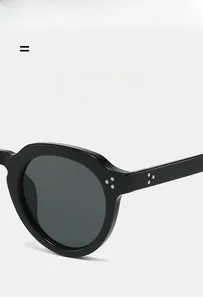 Close-up of black oval sunglasses featuring silver metal rivets and polished PC frame detail