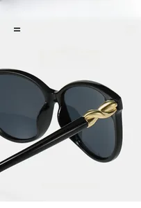 Close-up of black frame sunglasses showing gold twisted metal hinge and texture details