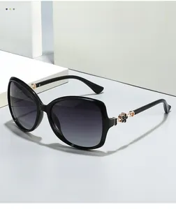 Detailed close-up of gold clover metal hinge and texture on black oversized sunglasses