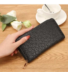 Detail of black long leopard embossed wallet with gold zipper on a wooden table