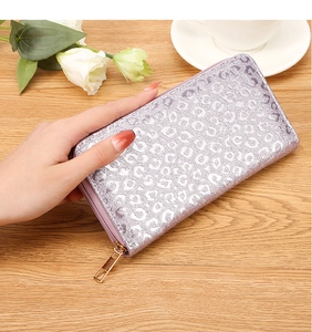 Detail of glitter silver leopard print wallet with golden zipper held over a tea set