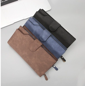 Three colors of matte leather long wallets stacked on a desk with a laptop