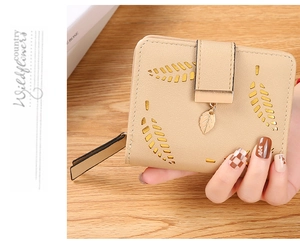 Close-up of beige leaf-cutout bifold wallet with golden leaf pendant and buckle