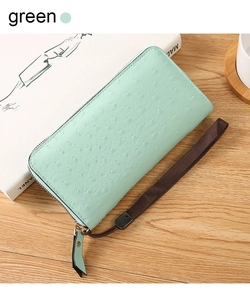 Detail of mint green ostrich-textured PU leather long wallet with wrist strap on wooden table