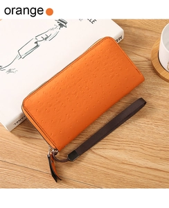 Detailed top view of an orange ostrich pattern clutch bag with silver zipper on wood table